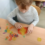Chłopiec w szarej bluzie układa kolorowe klocki geometryczne w kształt kropki na szkolnej ławce..jpg