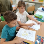 Dwaj chłopcy przy biurku pracują nad kartką z rysunkiem koszulki wypełnionej kolorowymi kołami..jpg