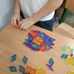 Dziecko w białej koszulce układa na ławce kolorowy wzór z magnetycznych klocków geometrycznych..jpg