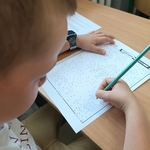 Chłopiec w białej koszulce łączy kropki ołówkiem na kartce z zadaniem..jpg