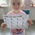 Dziewczynka w różowej koszulce prezentuje wypełnioną kartę pracy Biegaj i pisz razem z kropką..jpg