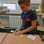 Chłopiec przy stole skleja kawałki makaronu spaghetti_ przygotowując element konstrukcji.jpg