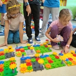Dzieci siedzą na podłodze i wspólnie porównują duże kolorowe konstrukcje z klocków.jpg