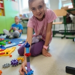 Uśmiechnięta dziewczynka w różowej bluzce prezentuje wieżę z kolorowych klocków.jpg