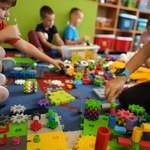 Dzieci siedzą na dywanie i budują tory przeszków z klocków Korbo.jpg