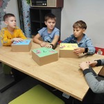 Czworo chłopców siedzących przy stole odgaduje za pomocą zmysłu dotyku_ jakie przedmioty ukryły się w pudełkach.jpg