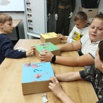 Czworo uczniów siedzących przy stole odgaduje za pomocą zmysłu dotyku_ jakie przedmioty ukryły się w pudełkach.jpg