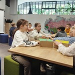 Uczniowie siedzący przy stolikach odgadują za pomocą zmysłu dotyku_ jakie przedmioty znajdują się w pudełkach.jpg