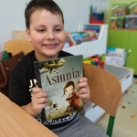 Chłopiec w klasie uśmiecha się_ trzymając książkę „Asiunia” Joanny Papuzińskiej..jpg