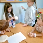 Grupa dzieci przy stole omawia pomysł na konstrukcję_ jedno z nich trzyma papierowy kubek..jpg