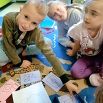 Troje dzieci siedzi na dywanie i układa rysunki przedstawiające różne przedmioty_ np. plecak i apteczkę..jpg