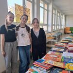 Na korytarzu szkolnym stoją trzy uczennice  Przed nimi ustawione w szeregu stoły z książkami..jpg