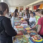 Przy ustawionych w szeregu stołach z książkami stoją uczniowie..jpg