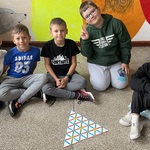 Piątka chłopców siedząca na podłodze prezentuje ułożoną łamigłówkę matematyczną.